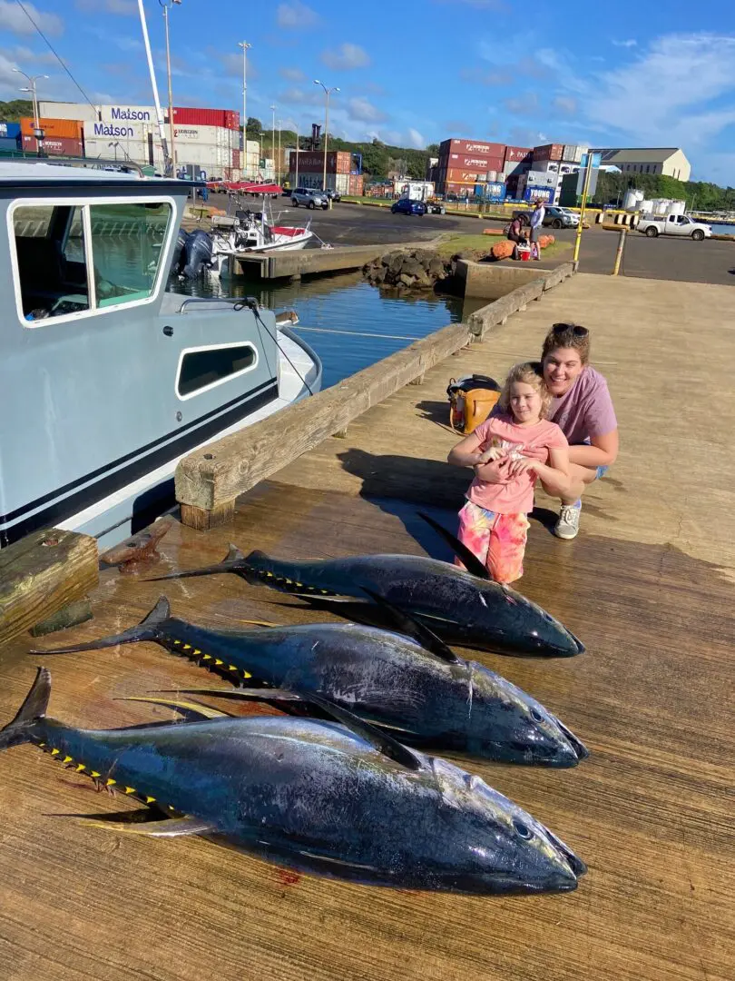 A woman and child standing next to fish on the dock.