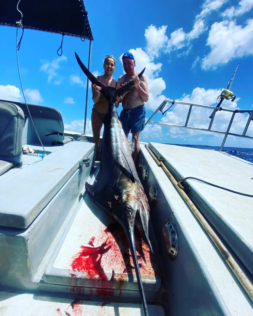 Two men standing on a boat with a dead fish.