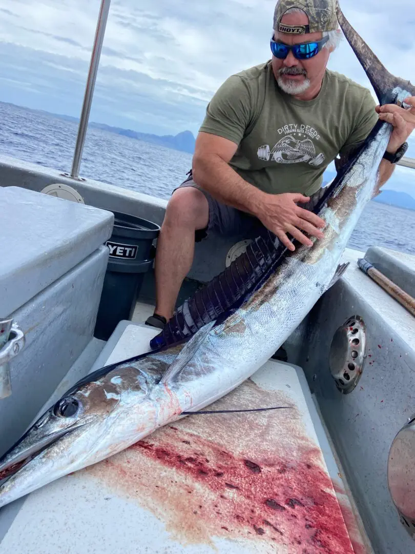 A man sitting on the back of a boat holding a large fish.