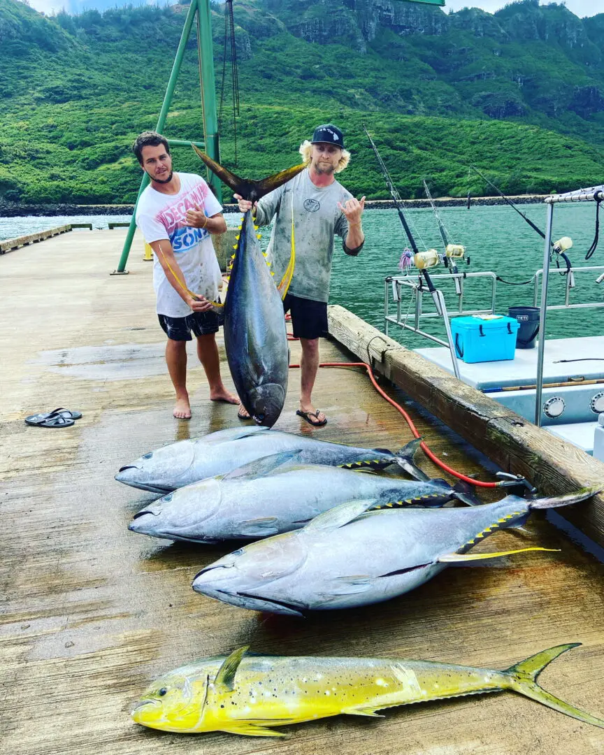 Two men standing on a dock holding onto tuna.