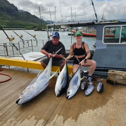 Two people displaying large caught fish dockside.