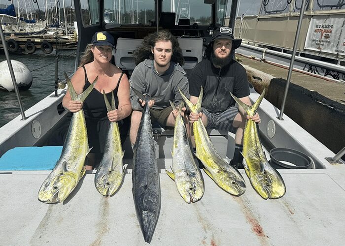 Three people on boat holding large fish.
